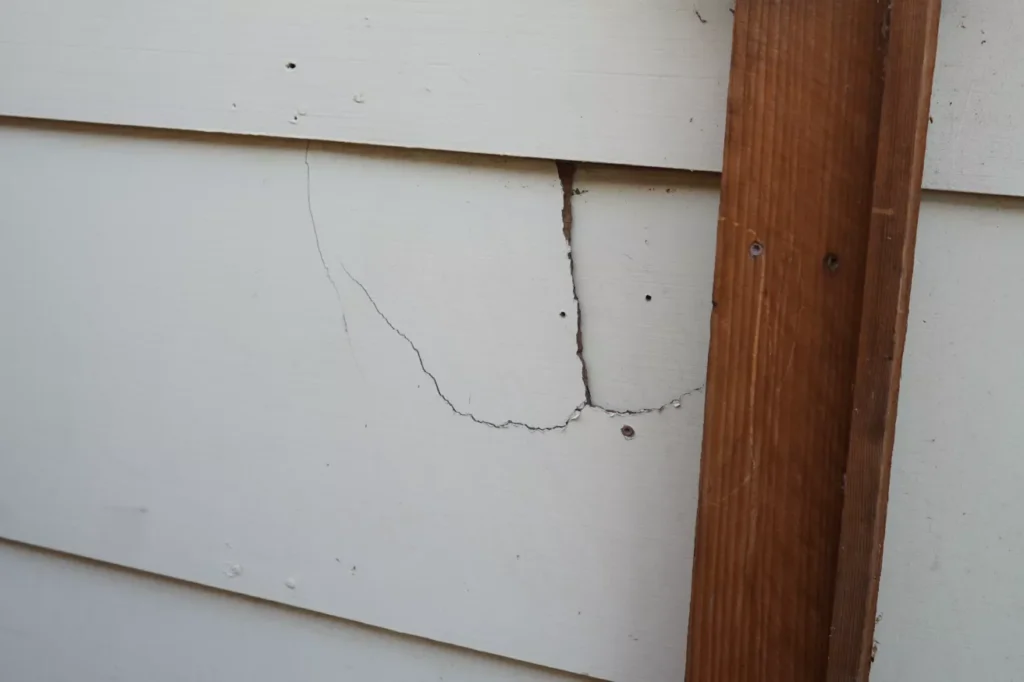 Contractor inspecting cracked siding panel for repair