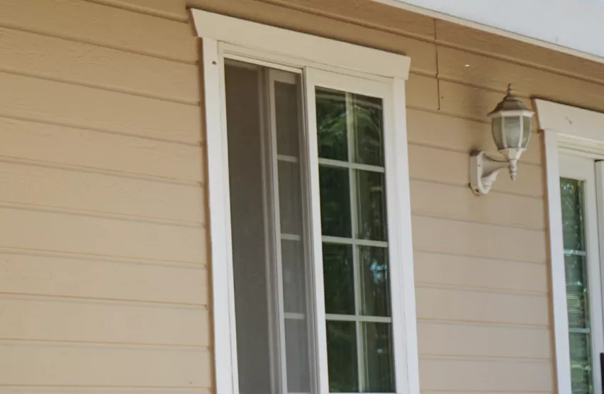 Older white-frame grid window beside a porch light before window replacement