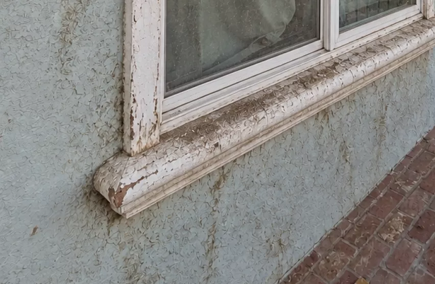 Worn, peeling window sill on a stucco wall before window replacement